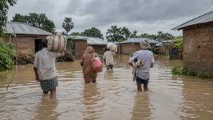 Personas adultas avanzan por una calle rural anegada bajo lluvia intensa hacia una zona segura.