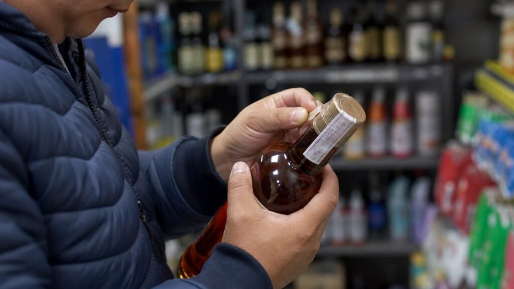 Persona revisa el sello y la tapa de una botella en una licorera genérica