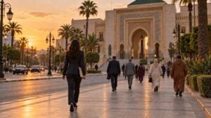 Peatones caminan por una avenida de Rabat al atardecer frente a un edificio de arcos y mosaicos de estilo marroquí.