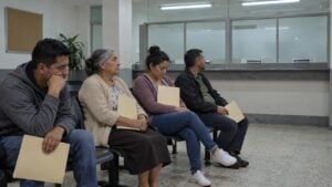 Personas adultas esperan con carpetas frente a una ventanilla cerrada en una oficina pública colombiana.