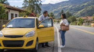 un taxi amarillo detenido en la vía entre dos municipios mientras el conductor habla con una pasajera.