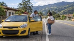 un taxi amarillo detenido en la vía entre dos municipios mientras el conductor habla con una pasajera.
