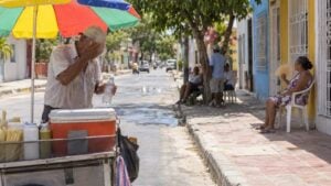 Vendedor ambulante se refresca con agua y una mujer se abanica en una calle soleada de Barranquilla.