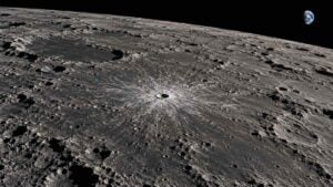 Cráter lunar reciente rodeado de material claro expulsado sobre una superficie gris con sombras largas.