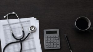 Fonendoscopio sobre hojas con tablas contables, junto a una calculadora y un esfero
