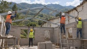 Cuatro obreros levantan el techo de una escuela rural, junto a un muro agrietado y montañas