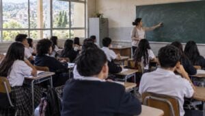 Una docente explica en el tablero a un grupo de estudiantes de secundaria en el salón de un colegio público.