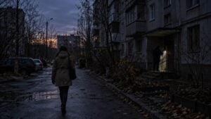 Una mujer camina de noche por una calle a oscuras mientras un vecino alumbra con una linterna.