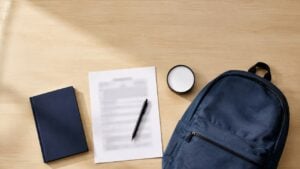 Formulario en blanco, un esfero, un cuaderno y un morral escolar azul sobre un escritorio de madera