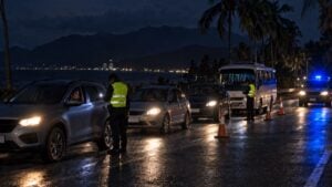Retén policial nocturno con vehículos detenidos en una carretera costera y montañas al fondo.