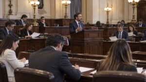 Congresistas ficticios revisan documentos durante una sesión en un salón legislativo genérico.