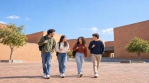 estudiantes universitarios caminan y conversan con morrales en una plazoleta de un campus colombiano con edificios de ladrillo y árboles.