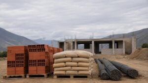 Ladrillos, bultos de cemento y varillas frente a una construcción en obra en una zona montañosa