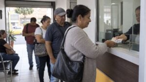 Una mujer recibe pesos en efectivo en la ventanilla de una oficina de giros mientras otras personas esperan en fila.