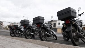 Hilera de motocicletas de trabajo con baúles parqueadas junto a un andén urbano