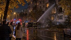 bomberos rocían agua sobre un edificio residencial dañado en Kiev de noche, con vecinos abrigados mirando desde la calle.