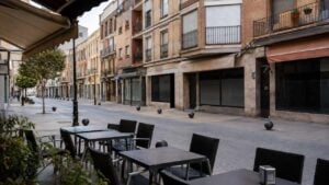Calle comercial española con balcones, toldos y una terraza de café vacía