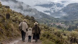 una familia campesina camina por un camino de montaña en Santander con el páramo y sus frailejones al fondo, bajo un cielo nublado.