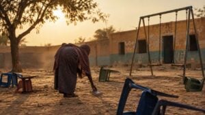Mujer de espaldas recoge un cuaderno en el patio polvoriento de una escuela rural del Sahel