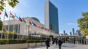 Delegados caminan hacia un complejo diplomático genérico de Nueva York con policías y tráfico al fondo.