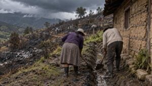 Dos campesinos limpian una zanja junto a su casa en una ladera quemada mientras se acerca la lluvia.