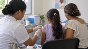 Enfermera vacuna a una niña acompañada por su madre en una sala de un centro de salud público.