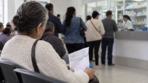 Una mujer mayor espera con su fórmula médica en la fila de una farmacia.