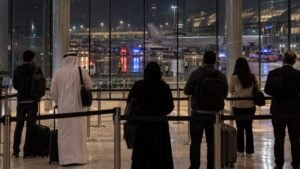 Pasajeros esperan detrás de una cinta de seguridad en la terminal de un aeropuerto, de noche, con luces de emergencia.