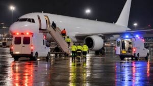 Ambulancias junto a un avión comercial estacionado de noche en un aeropuerto.