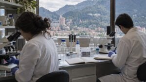 Una investigadora y un investigador trabajan con microscopios y cuadernos en un laboratorio universitario.