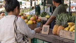 Una clienta paga con su celular en un puesto de frutas de una plaza de mercado.
