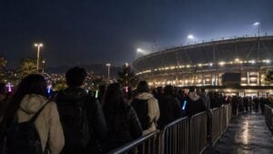Fans hacen fila de noche frente a la entrada de un estadio en Bogotá con barras de luz.