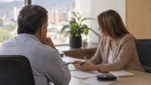 Un hombre conversa con una asesora en la oficina de una entidad financiera, con una calculadora sobre el escritorio.