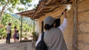 Técnica de salud revisa con una linterna las grietas de una casa rural junto a una familia campesina.