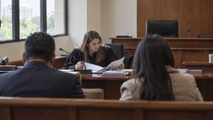 Una mujer con toga revisa documentos en el estrado de una sala de audiencias