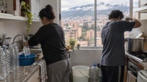 Dos personas almacenan agua en botellas y ollas en la cocina de un apartamento antes de un corte.