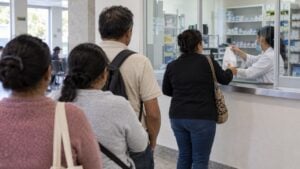 Pacientes hacen fila frente a la ventanilla de entrega de medicamentos de un hospital.