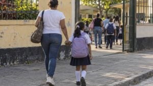 Una madre y su hija con uniforme llegan a la entrada de un colegio público por la mañana.