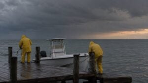 Dos personas aseguran una lancha en un muelle mientras se acercan nubes de tormenta sobre el mar.