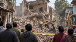 Rescatistas remueven escombros de un edificio de ladrillo mientras varios vecinos observan desde un callejón.