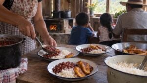 Una mujer sirve arroz, fríjoles y plátano mientras una familia espera al fondo de una cocina rural.