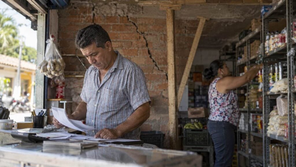 Dueño de un local revisa papeles junto a una pared agrietada y un techo apuntalado