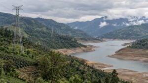 Torres de alta tensión cruzan montañas verdes junto a un embalse con el nivel bajo.