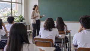 una profesora habla con estudiantes de bachillerato en un salón de clases de un colegio público.