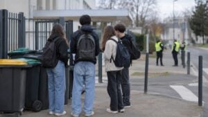 estudiantes reunidos frente a un liceo francés junto a contenedores apilados, con policías a lo lejos.
