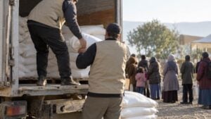 Trabajadores humanitarios descargan sacos de harina mientras familias esperan en fila en Gaza.