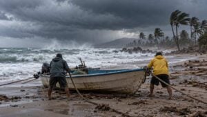 Dos pescadores de espaldas aseguran una lancha ante el fuerte oleaje y las palmeras agitadas.