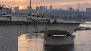 rescatistas revisan el tablero dañado de un puente de concreto sobre un río en Kiev al atardecer.