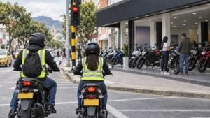 motociclistas con casco esperan en un semáforo frente a un concesionario con motos nuevas alineadas en la acera.