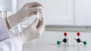 Una química sostiene un frasco en un laboratorio junto a dos modelos de moléculas que son imagen en espejo.